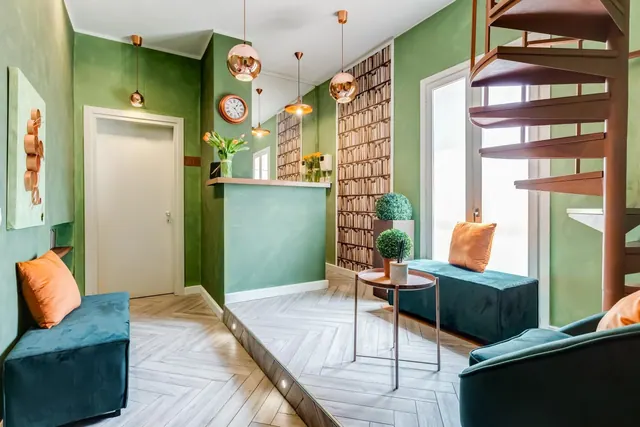 A green-walled lounge area with teal velvet benches, copper pendant lights, a spiral staircase and a herringbone wood floor.
