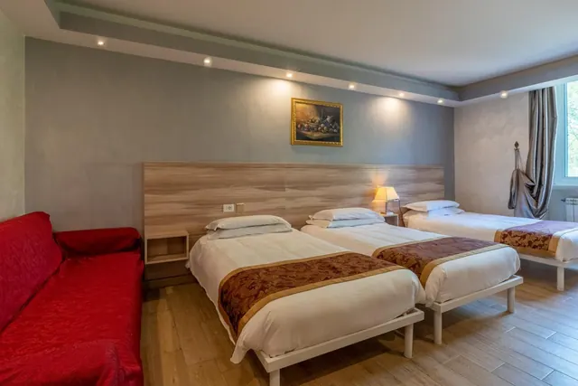 A hotel bedroom with three single beds, a red sofa on the left, a framed painting on the wall and a wood-panelled headboard.