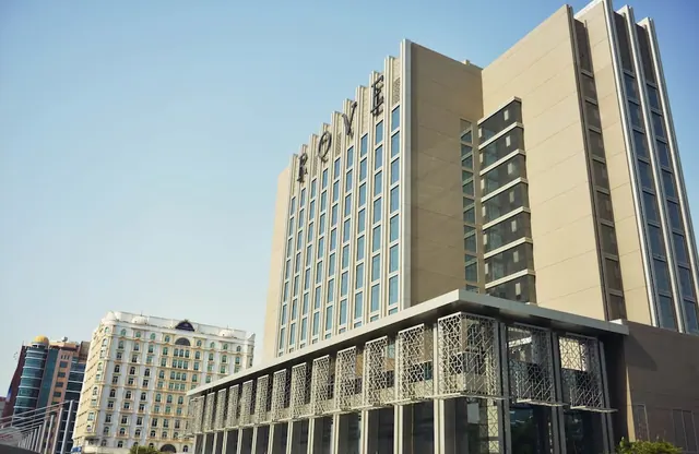 The exterior of a tall beige hotel tower with the name ROVE on its facade, a lower glass-and-metal entrance structure in front, and a clear blue sky above.