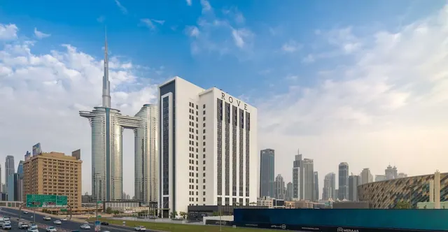 Exterior of the Rove hotel tower with neighbouring skyscrapers behind it, and a highway with traffic in the foreground under a partly cloudy sky.