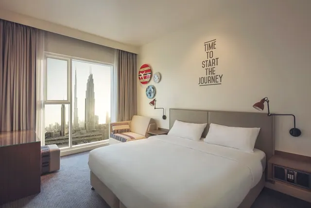 A hotel bedroom with a made double bed, an armchair and a large window overlooking the Burj Khalifa and city skyline.