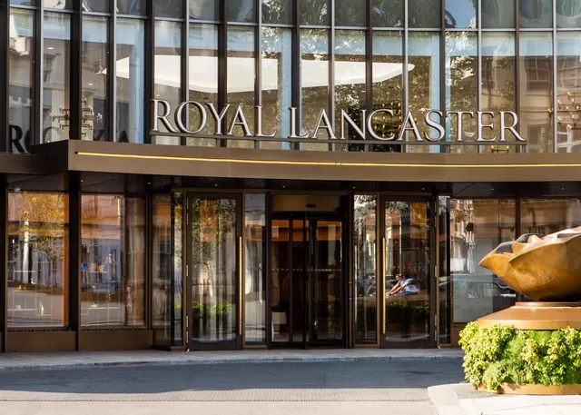 The front entrance of the Royal Lancaster hotel, with its name in large letters across the glass facade and a gold sculpture beside the doors.