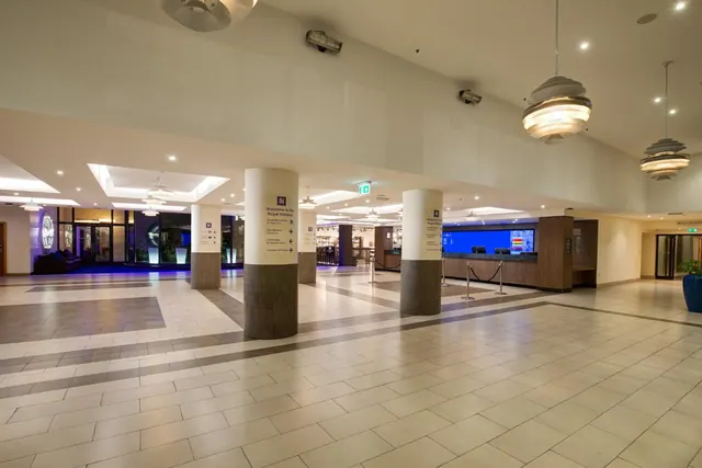 An empty lobby with a tiled floor, pillars, pendant lights and a reception desk with a blue display screen.