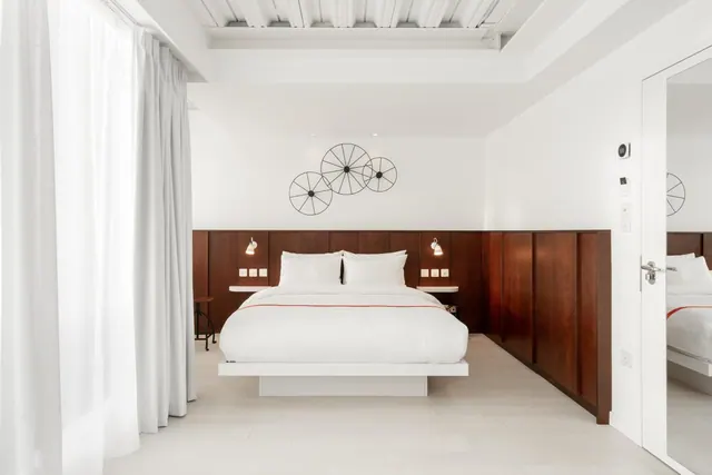 A bedroom with a king bed with white bedding, dark wood wall panelling behind the headboard, and a metal wheel wall decoration.