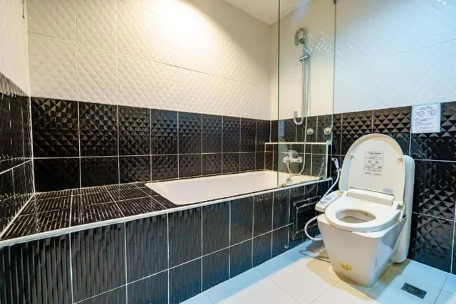 A bathroom with a built-in bathtub, a glass-screened shower, and a toilet with a bidet wand, set against black and white textured tiles.