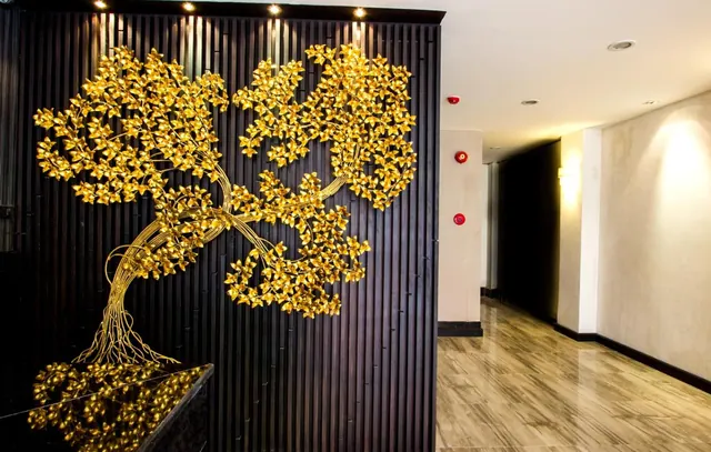 A gold-coloured metal tree sculpture is mounted on a dark slatted wall beside a corridor with a polished stone-look floor and red fire alarms on the wall.