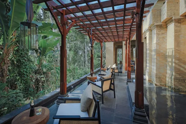 A covered terrace with a wooden pergola, cushioned armchairs and side tables, overlooking dense tropical greenery.