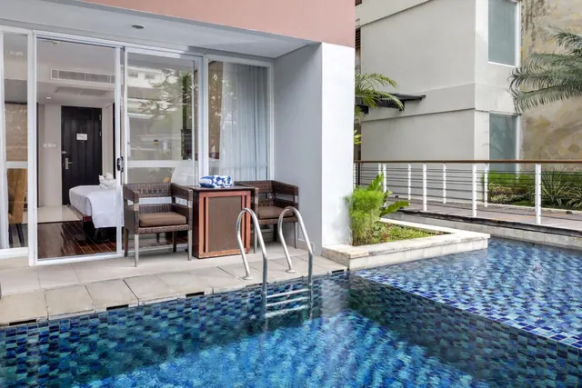A small private plunge pool lies beside a terrace with wicker chairs and a side table, outside sliding glass doors that open onto a bedroom with a bed.