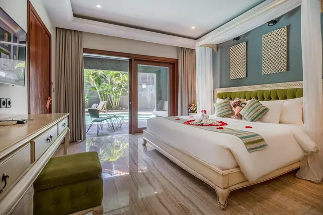 A bedroom with a canopy king bed, a wall-mounted television, and sliding doors opening onto a private pool and tropical garden.