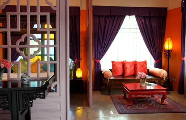 A room with purple drapes, a daybed with red cushions, a red coffee table and a carved lattice screen in the foreground.