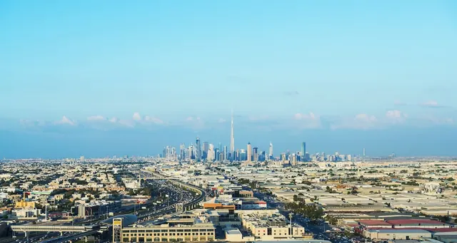 Aerial view over a sprawling Dubai cityscape with the Burj Khalifa rising on the skyline under a clear blue sky.