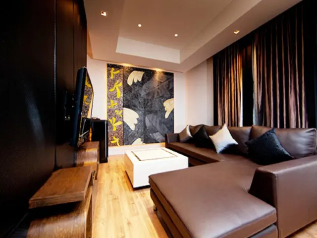 A living room with a brown leather L-shaped sofa, a wall-mounted television, a white coffee table and dark curtains.