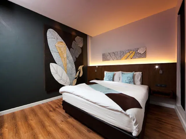 A bedroom with a double bed under a wall of stylised leaf artwork, a backlit wooden headboard, and wood-effect flooring.