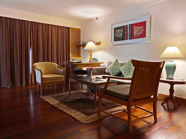 A hotel suite living area with a sofa, two armchairs, a writing desk, a coffee table and two table lamps.