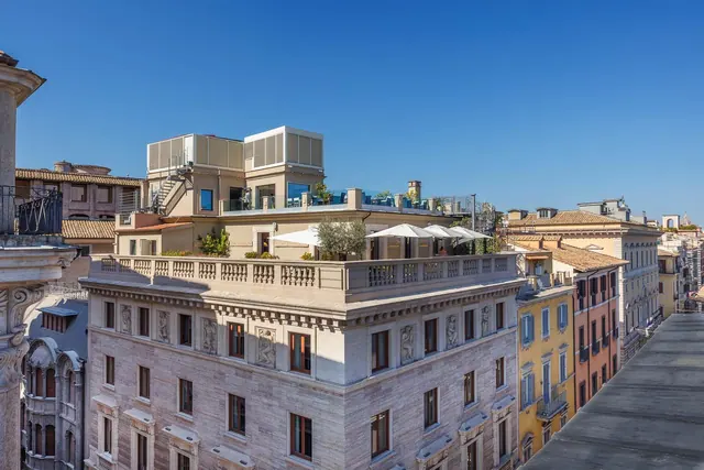 A view across neighbouring Rome rooftops and older facades, with white umbrellas and rooftop structures on the hotel terrace in the foreground.