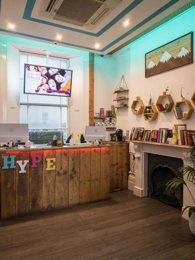 A reception area with a wooden front desk, a wall-mounted television, shelves of books and a white fireplace.