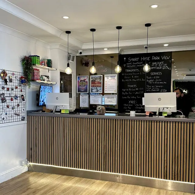 A reception desk with two computer monitors, a chalkboard information board and pendant lights, with a staff member partly visible behind the counter.