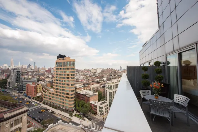 A rooftop terrace with a round table, four chairs and topiary plants overlooks a city skyline with the Empire State Building visible on the left.