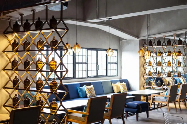 A lounge area with a blue built-in banquette, wooden armchairs, pendant lights and amber bottles displayed on lattice shelving.