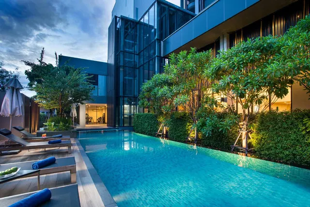 A lap pool beside a glass-fronted building with sun loungers, rolled blue towels and a plate of fruit at dusk.