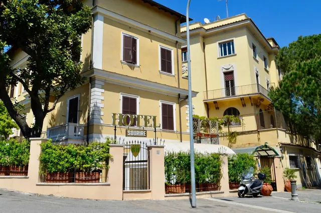 The yellow exterior of Hotel Sourire with its name sign, a gated front wall and a parked scooter on the street.