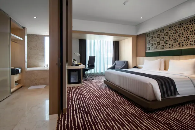 A king bed, work desk, armchair and built-in bathtub are visible in a bedroom with tall windows and a view through to the bathroom.