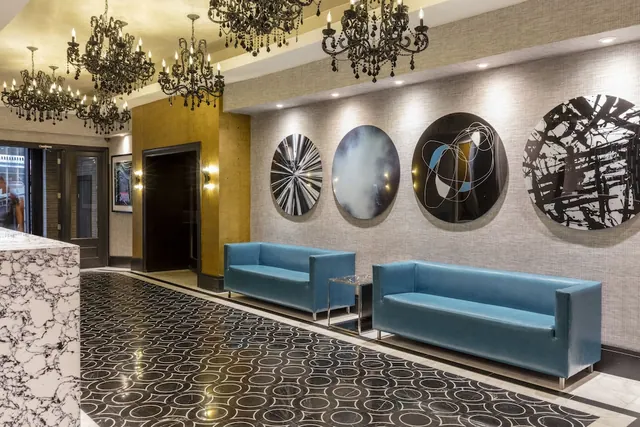 A lobby with black crystal chandeliers, a marble reception counter, two blue sofas and round wall artworks.