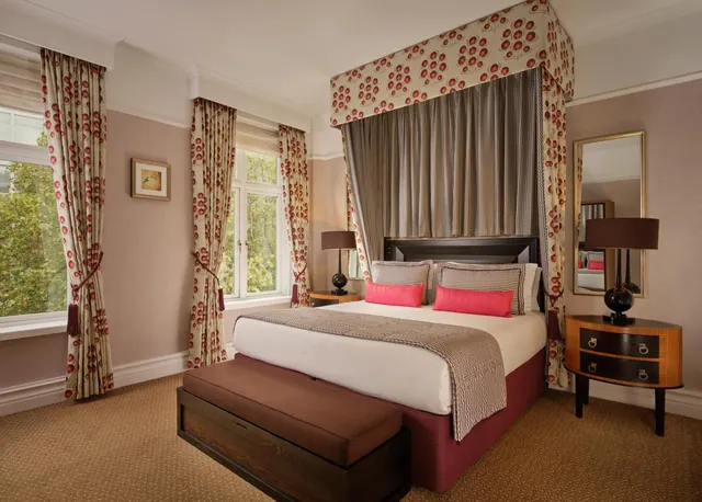 A bedroom with a canopy bed dressed in red and white patterned fabric, with two windows looking onto trees.