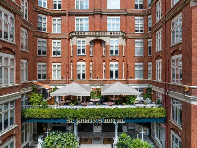 A red brick courtyard building with white umbrellas over outdoor dining tables and the St Ermin's Hotel entrance sign below.