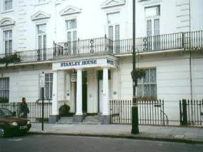A white building with a columned entrance portico and a sign reading Stanley House, seen from the street with a parked car and a pedestrian on the left.
