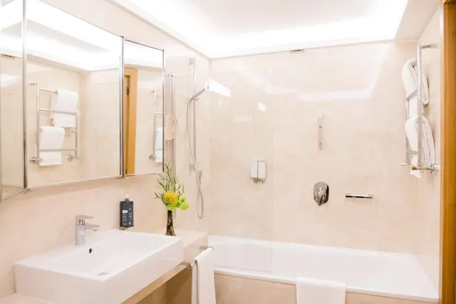 A bathroom with a white basin on a wall-mounted counter, a mirror cabinet, heated towel rails, and a bathtub with a glass shower screen.