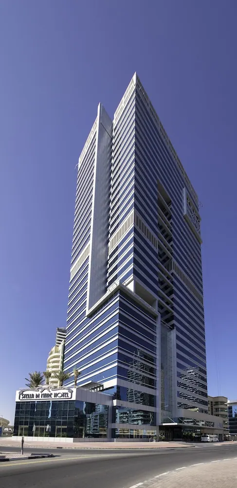 Low-angle view of a tall blue glass hotel tower with a Stella Di Mare Hotel sign at its base under a clear blue sky.