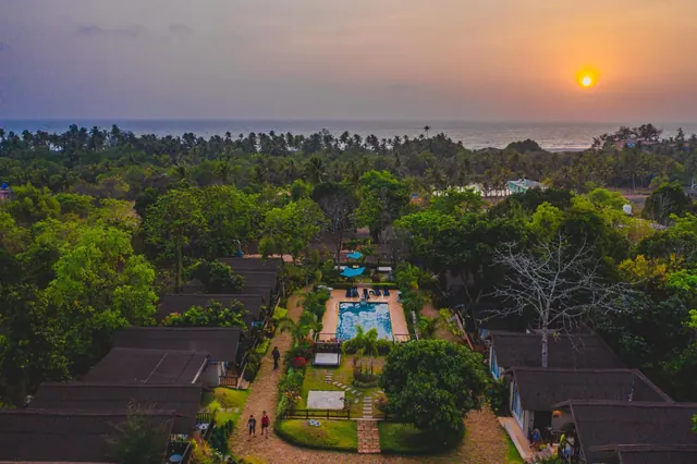 An aerial view shows the tropical property, swimming pool, gardens, and sea at sunset.