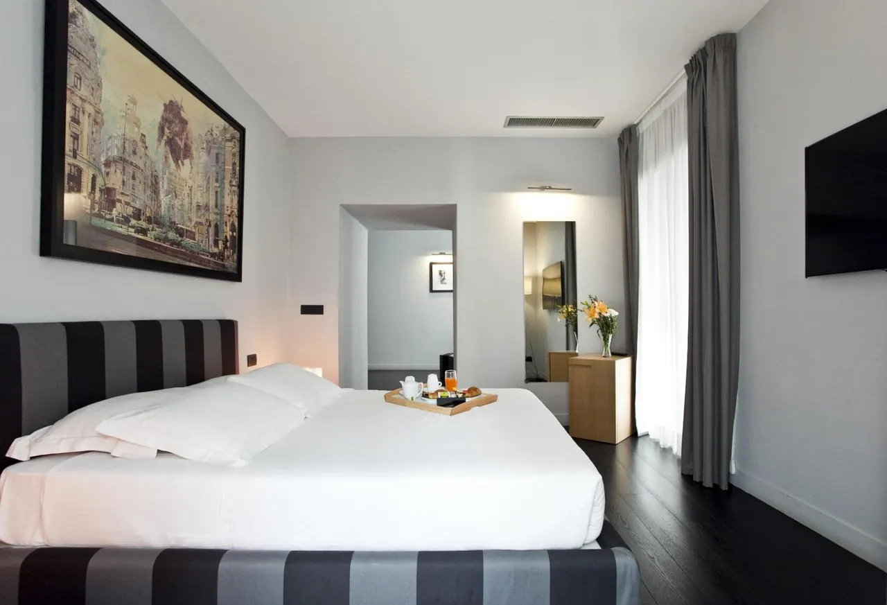 A made king bed with a striped upholstered headboard, a breakfast tray on the bed, a large framed artwork on the wall, and a wall-mounted television.