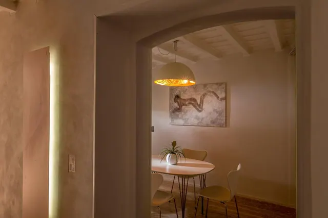 An arched doorway opens onto a dining area with an oval table, several chairs, a pendant lamp, and a framed artwork on the wall.