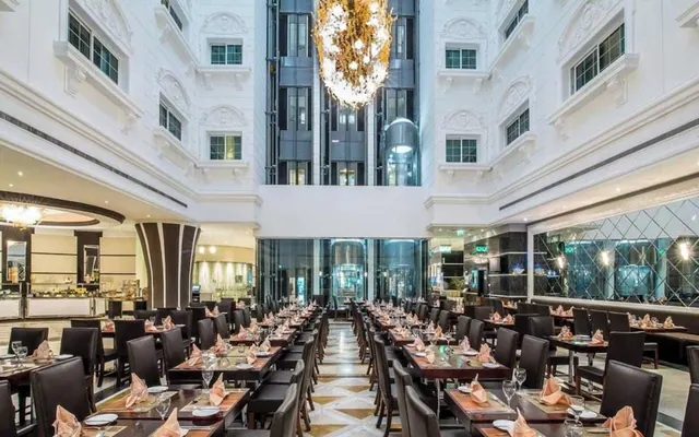 A large dining room with rows of set tables, dark leather chairs, a tall white atrium and a large chandelier hanging from the ceiling.