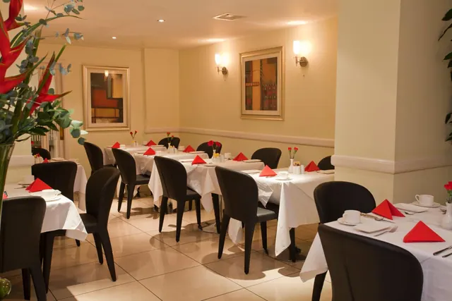 A restaurant dining room with white-clothed tables, red napkins, black chairs, wall sconces and framed paintings on the walls.