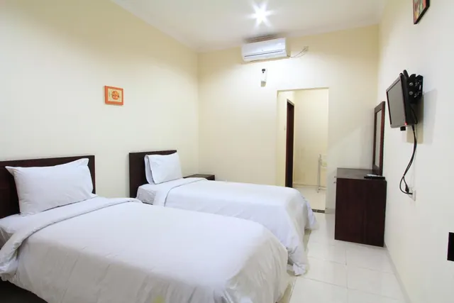 A bedroom with two single beds made with white linen, a wall-mounted air conditioner, and a wall-mounted television on the right wall.