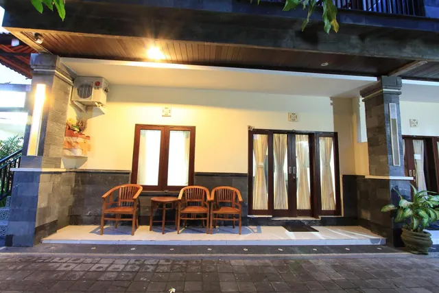 A covered ground-floor terrace with four wooden chairs and a small table sits in front of glass doors with curtains, and a wall-mounted air conditioner unit is fixed beside them.
