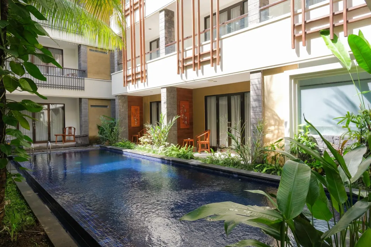A rectangular lap pool in an inner courtyard is surrounded by hotel room doors, balconies and tropical plants.