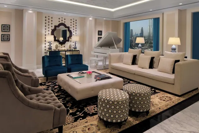 A large living room with a cream sofa, tufted armchairs, a white grand piano and a window view of the Burj Khalifa and city skyline.