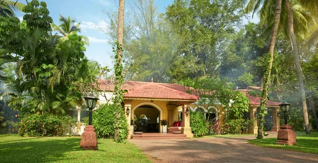 A tiled-roof heritage-style building stands amid a landscaped tropical garden with palm trees and a central paved approach.