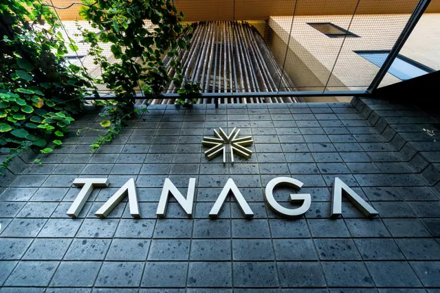 Entrance courtyard with the TANAGA name in raised letters and a star emblem on a tiled floor, with climbing vines and a mesh-covered stairway beside it.