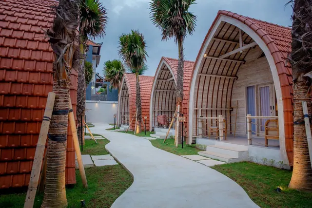 A paved path runs between arched bungalows with terracotta tile roofs and palm trees at dusk.