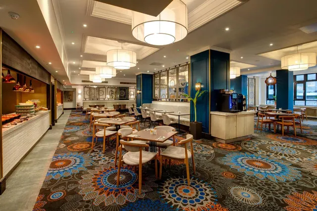 A restaurant dining room with set tables and wooden chairs, a buffet counter on the left and a coffee machine on a counter on the right.