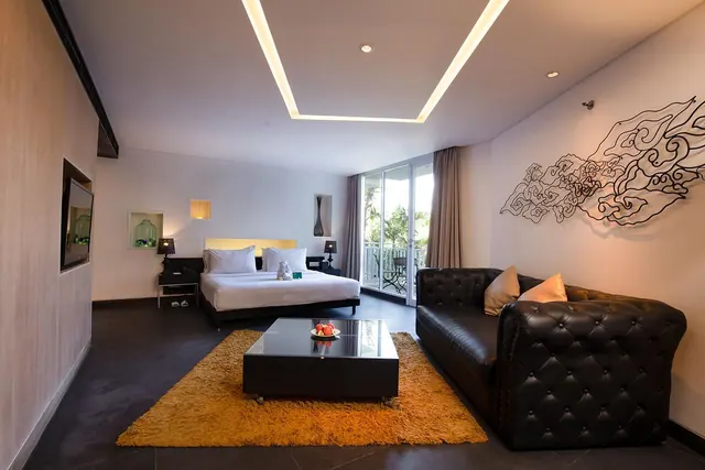 A bedroom with a king bed, a black tufted leather sofa, a coffee table with a fruit bowl, and glass doors opening onto a balcony with palm trees outside.