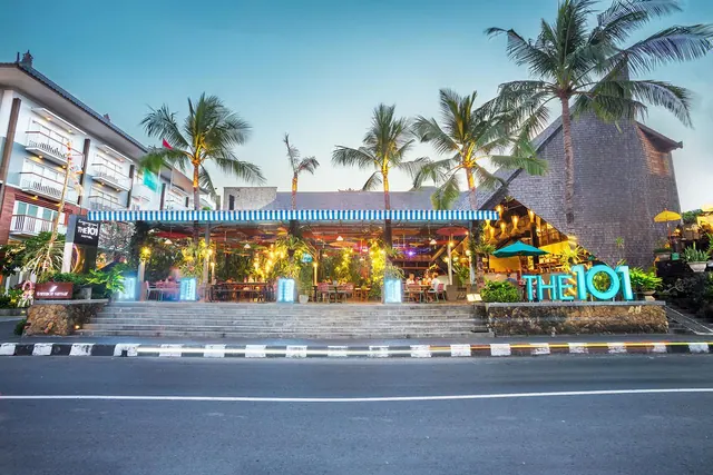 Exterior of The 101 restaurant at dusk, with steps up to an open dining area under a striped awning and palm trees beside the street.