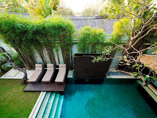 Overhead view of a private swimming pool with sun loungers on a timber deck, bamboo screening and a lawn beside it.