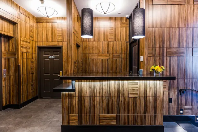 A lobby with wood-veneer walls, a dark reception counter with a vase of yellow flowers, two pendant lights and a door with a small staff-only sign.