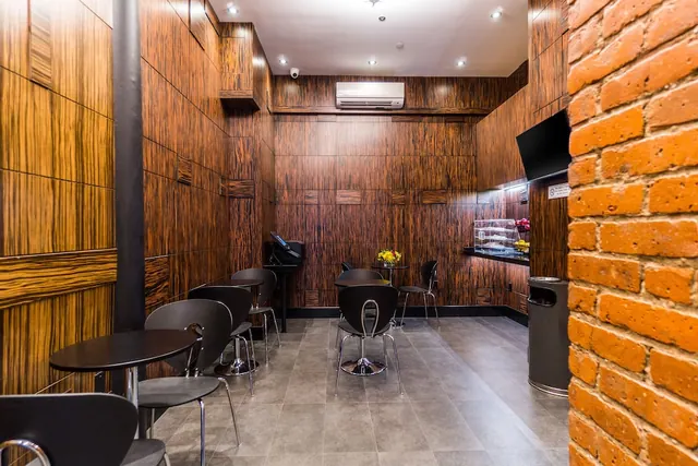 A small café-style dining area with dark wood-panelled walls, black chairs and tables, a wall-mounted air conditioner, a wall-mounted television and a brick column in the foreground.